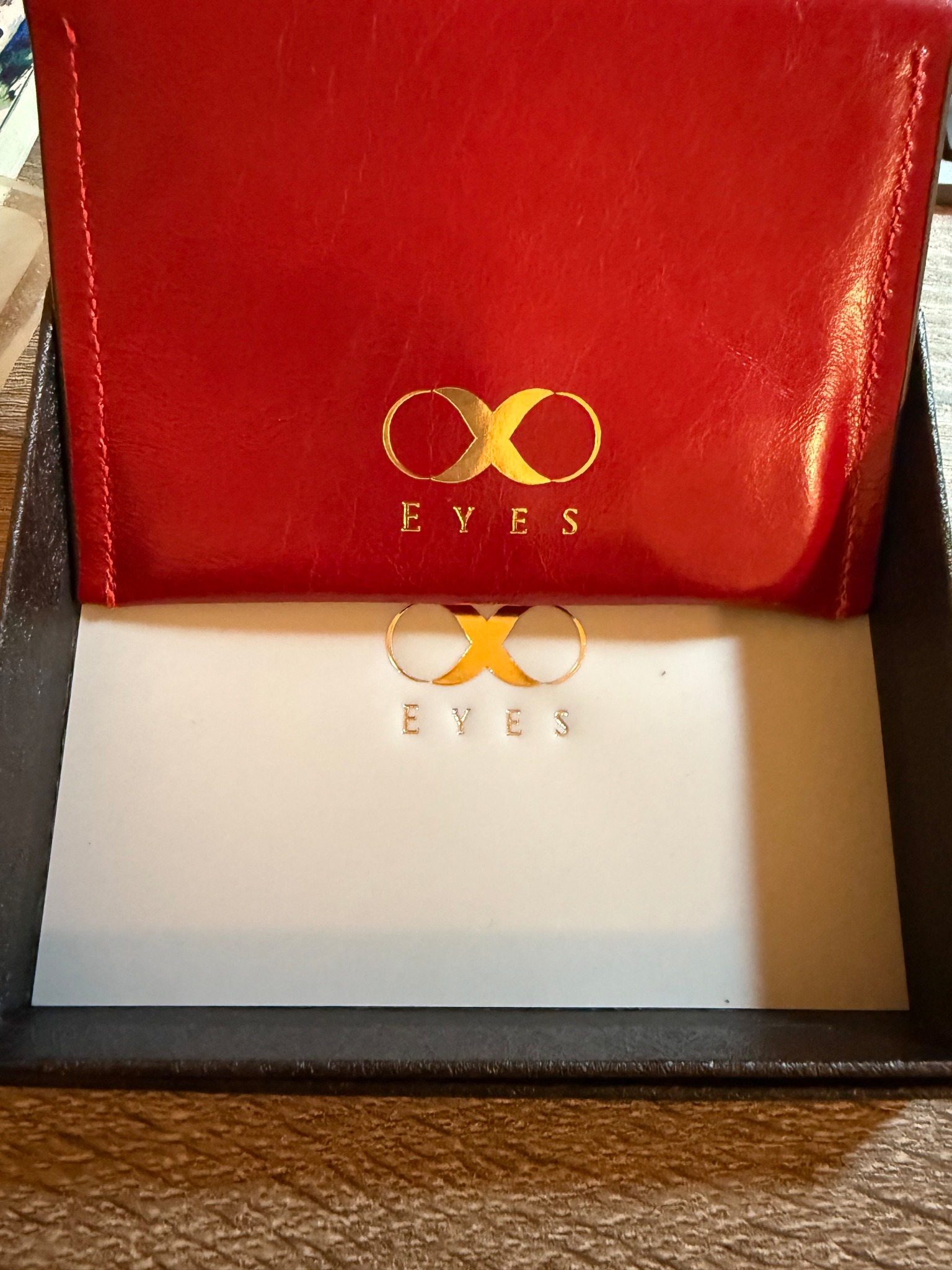 紅色皮革零錢包打開，金燙 EYES 無限符號，旁邊搭白色名片卡